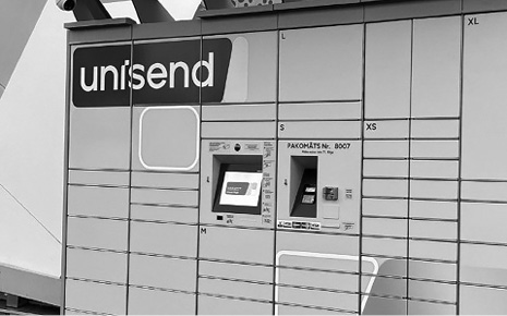 . Посылочный автомат, вверху слева видим логотип действующей в странах Балтии службы доставки UNISEND. Над окошком выдачи/отправления расположена более мелкая надпись латиницей PAKOMĀTS (латышский язык), Латвия