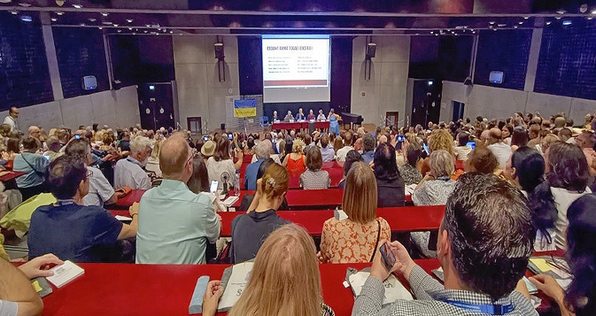 На изображении представлено пленарное заседание во время открытия XVII Международного съезда славистов в Сорбонне (Париж, 25 августа 2025 г.). В зале много слушателей. Сбоку размещён баннер в поддержку Украины.