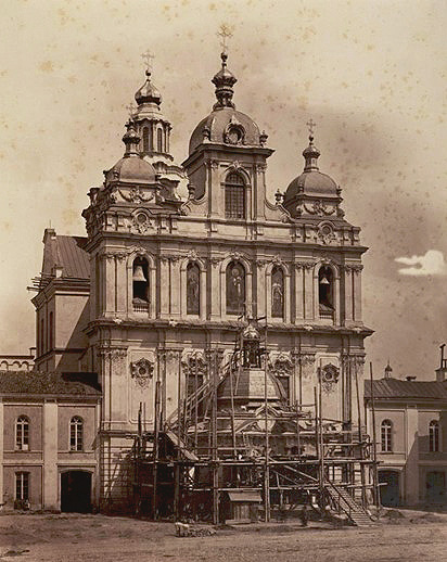 A historic baroque-style building with ornate towers and scaffolding around a central dome under restoration.
Description generated by AI