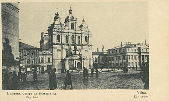A historic city square with a large ornate baroque-style church in the center, surrounded by several people walking and standing on a cobblestone street.
Description generated by AI