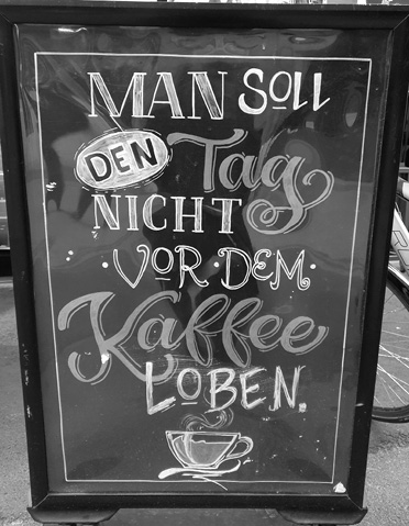 A chalkboard sign with decorative lettering in German reads "Man soll den Tag nicht vor dem Kaffee loben" with a drawing of a steaming coffee cup at the bottom.

Description generated by AI