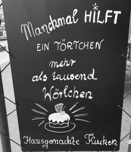 A chalkboard sign with handwritten German text promoting homemade cake with a small drawing of a cake on a plate.

Description generated by AI