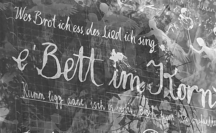 A wall with handwritten German text in white paint surrounded by faint images of dancing figures and foliage.

Description generated by AI